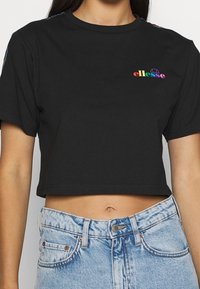 Camiseta negra recortada con mangas cortas, que presenta un logo "ellesse" multicolor en el lado izquierdo del pecho y acentos a rayas en contraste en los hombros.