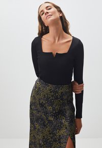 Zwarte long-sleeve top met een vierkante halslijn, gecombineerd met een kokerrok tot de knie met een groen en zwart luipaardprintpatroon en een zijsplit.