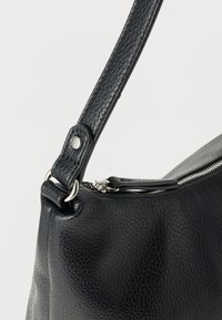 Μαύρη δερμάτινη τσάντα με υφή, με ασημένιο φερμουάρ και λουρί προσαρτημένο με μεταλλικό κρίκο και λεπτομέρειες με πριτσίνια, πάνω σε λευκό φόντο.