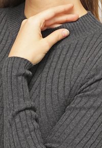 Maglione grigio a costine con collo alto e maniche lunghe, caratterizzato da una texture morbida e variazioni sottili nel motivo dei punti.