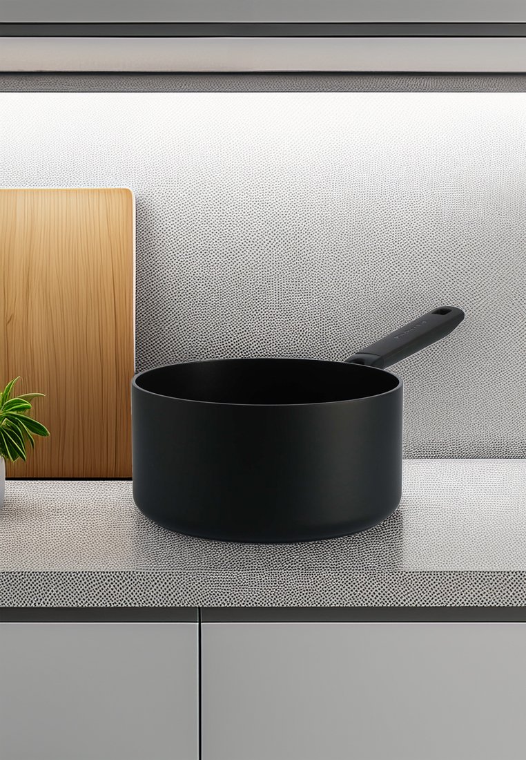 Czarny garnek kuchenny z gładkim matowym wykończeniem i solidną rączką, umieszczony na teksturowanym blacie obok drewnianej deski do krojenia i rośliny.