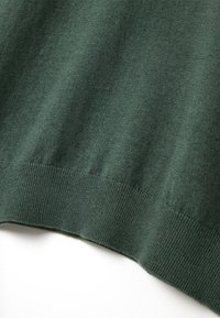 Dunkelgrüner Strickpullover mit glatter Textur und ribbeltem Saum. Der Stoff wirkt weich und leicht mit einem schlichten Design.