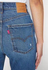 Jean en denim à taille haute, de couleur bleu clair, coutures visibles et un patch en cuir portant l'inscription "Levi Strauss & Co." à l'arrière.