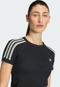 Czarna dzianinowa koszulka z białymi paskami na ramionach, okrągłym dekoltem i krótkimi rękawami, z logo Adidas na piersi.