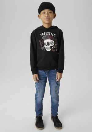 Sweatshirt à capuche noir avec un graphique de skull coloré et du texte ; associé à un pantalon en denim bleu clair avec des poches cargo ; sneakers noirs.