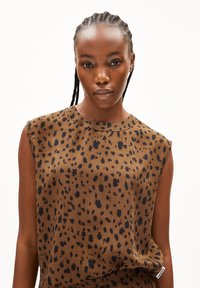 Brown sleeveless top with black leopard spots, made of smooth fabric, featuring a round neckline and subtle stitching detail on the shoulders.