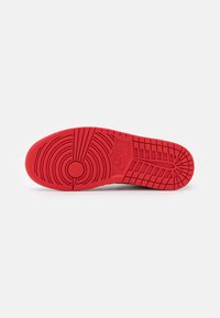 Semelle en caoutchouc rouge d'une chaussure Nike avec des motifs de bande de roulement circulaires et rectangulaires, présentée sur fond blanc.