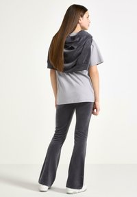 Grå t-shirt med korte ærmer, parret med grå velour-bukser med vidde. Et gråt hættetrøje hviler afslappet på skuldrene.