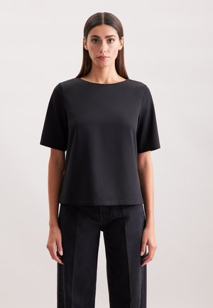 Top nero a maniche corte con scollatura rotonda, texture liscia e vestibilità ampia, abbinato a jeans scuri a vita alta.