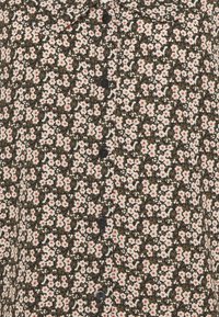 Camicia nera con stampe floreali, caratterizzata da un motivo di fiori bianchi e rossi su uno sfondo scuro. I bottoni sono neri e uniformemente distanziati.