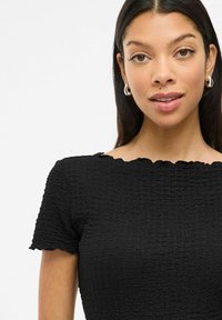 Top negro texturizado con mangas cortas, que presenta un escote con forma de ondas y un diseño fruncido. Vista del torso superior, la tela parece elástica.