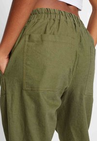 Olivinvihreät, kevyet housut, joissa on joustava vyötärönauha, kaksi takataskua ja sileä pinta.