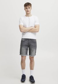 Grå denimshorts med rullekanter, brukt sammen med en enkel hvit T-skjorte, kombinert med mørke sneakers og hvite ankelsokker. Enkelt design.