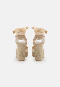 Sandali con zeppa in tessuto beige intrecciato, dettagli crema e tacco avvolto in corda. Le cinghie presentano fiocchi alla caviglia.