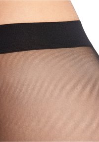 Fascia nera sopra collant trasparenti color marrone chiaro con una texture liscia, che mostra un fine e sottile motivo su tutta la superficie.