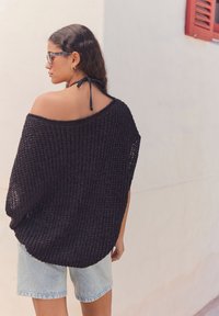 Maglione nero lavorato a maglia oversize con tessuto a rete aperto, scollatura rotonda e spalle basse, abbinato a pantaloni corti in denim chiaro.