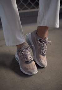 Light beige athletic shoes with a mesh upper, pink detailing, and a transparent Air sole. Features black glitter accents on the laces.