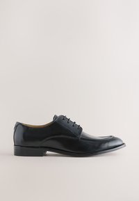 Chaussure habillée pour homme en cuir noir poli avec fermeture à lacets et petit talon sur un fond clair uni.