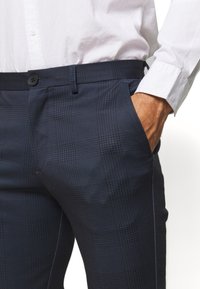 Kalhoty námořnického vzoru s kostkami z hladké tkaniny, s přizpůsobeným střihem, s bočními kapsami a zapínáním na knoflíky v pase.