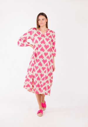 Robe beige fluide avec des motifs de feuilles roses, décolleté en V et manches 3/4. Assortie avec des sandales roses nouées pour un look coordonné.