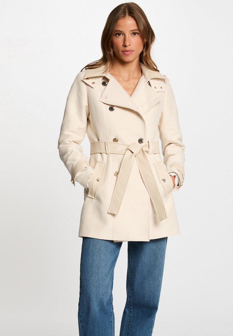 Manteau trench beige ceinturé avec un design croisé, grand col et poches latérales, fabriqué dans un tissu lisse.