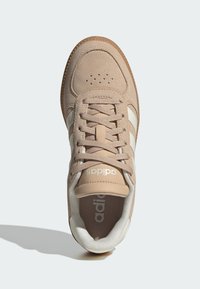 Beige mockasneakers med vita ränder, rundad tå, vadderad plös, perforeringar på vristen och texturerad gummisula.