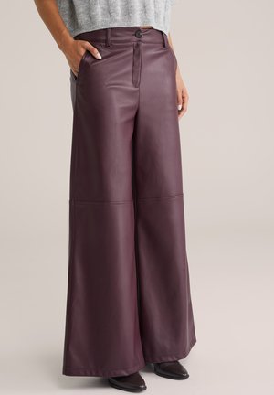 Woman wearing high-waist wide-leg burgundy leather pants with front button and zipper, paired with dark pointed shoes and gray sweater.