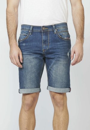 Donkerblauwe denim shorts met een vervaagde afwerking. Voorzien van opgerolde manchetten, voorkeurszakken en subtiele slijtage. Klassiek vijf-zakken ontwerp.