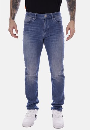 Jeans in denim chiaro con vestibilità dritta, cinque tasche e chiusura con bottone metallico. Indossati con sneakers bianche, mostrati frontalmente.