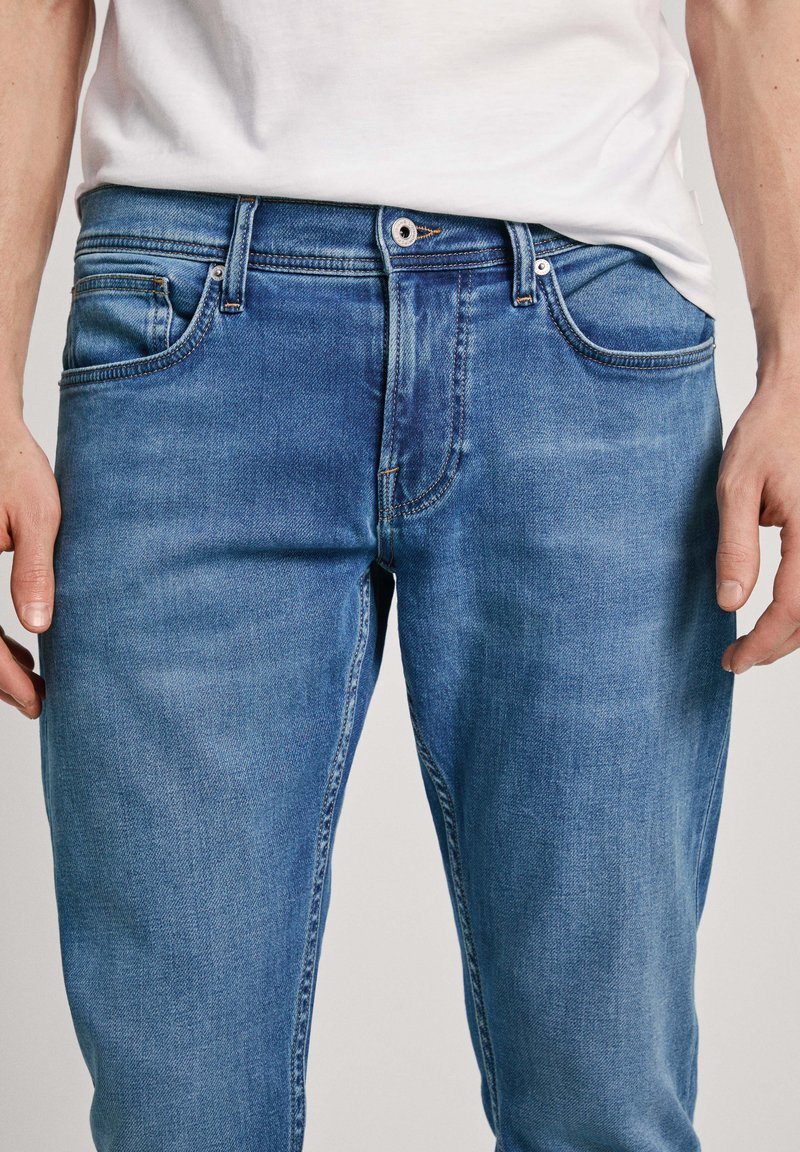 Jeans de mezclilla azul claro que presentan un diseño clásico de cinco bolsillos, un ligero efecto de desgaste y un cierre estándar de botón y cremallera.