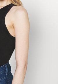 Body nero a coste con scollatura alta e aperture per le braccia. Texture liscia. Abbinato a jeans blu a vita alta.