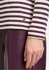 Bordeauxrode en witte gestreepte long-sleeve shirt met een klein rond logo aan de onderrand, gecombineerd met effen bordeauxrode leren broek.