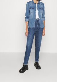 Denimskjorta i ljusblått med knäppning framtill, två bröstfickor och upprullade ärmar, tillsammans med mid-blå jeans och svarta platåstövlar.