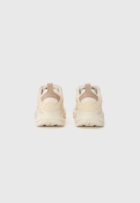 Beige Sport Schuhe mit einer strukturierten Oberfläche, gepolstertem Kragen und einer strapazierfähigen Gummisohle mit einem einzigartigen Profil.