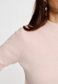 Helles rosa, strukturiertes Sweater mit hohem Kragen und langen Ärmeln. Auffälliger weicher Stoff und dezente Details entlang der Nähte.
