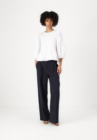 White puff-sleeve top with a peplum waist, complemented by navy wide-leg trousers. The fabric appears smooth, providing a structured silhouette.