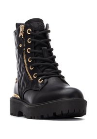 Bottine en cuir noir avec texture matelassée, fermetures éclair dorées, bout rond et semelle en caoutchouc noir épaisse avec un motif de crampons profonds.