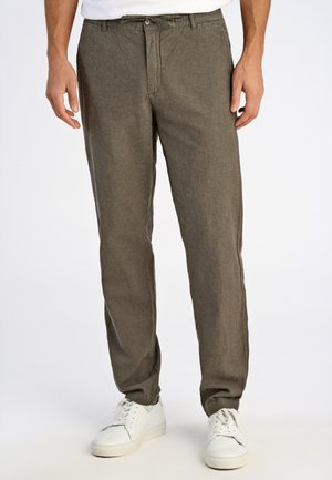 Pantalons en lin marron à coupe décontractée, dotés d'une fermeture à bouton et à zip, de poches latérales et de chevilles retroussées. Portés avec des baskets blanches.