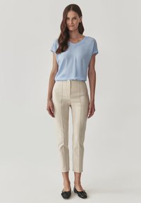 Top azzurro chiaro a maniche corte con scollo a V e dettagli tessuti, abbinato a pantaloni attillati crema a vita alta e scarpe flat nere.
