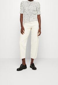 Top bianco a pois con maniche a sbuffo corte, abbinato a pantaloni diritti color crema e scarpe nere con lacci. Design semplice e moderno.