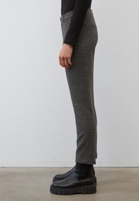 Pantalon gris à motif chevrons avec une coupe slim, taille haute et une poche latérale. Associé à des bottes noires à semelle compensée épaisse.