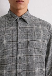 Grijze geruite shirt met een button-down kraag, twee voorste knopen en een gestructureerde stof met een patroon van zwart-witte geblokte lijnen.