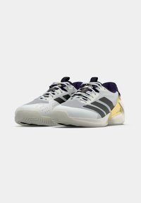 Białe buty sportowe z szaro-czarnymi akcentami, teksturowana siateczka, poduszka wokół kostki oraz złote akcenty na pięcie, z gumową podeszwą.