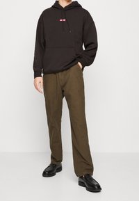 Zwarte hooded sweatshirt met een voorzak en rood logo, gecombineerd met bruine geruite broeken en zwarte leren schoenen.