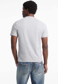 Grå kortærmet t-shirt med rund hals, lavet af bomuld. Bæres med blegede blå jeans med synlige sømme og baglommer.