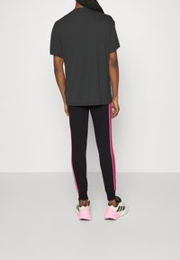 Person standing with back turned wearing a black t-shirt, black pants with pink stripes, and white sneakers with pink soles.