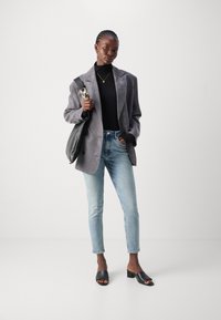 Blazer grigio in suede sopra un dolcevita nero, abbinato a jeans azzurri chiari e mules nere con apertura. Borsa nera con tracolla a catena.