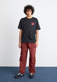 Sort grafisk t-shirt med rød tryk, røde løstsiddende bukser og sorte sneakers. Cirkulær sort crossbody taske med justerbar rem.