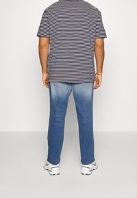 Randig marinblå T-shirt i kombination med ljusblå jeans, som har en avslappnad passform och subtila blekningar. Vita sneakers fulländar stilen.