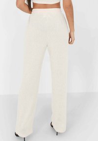 Pantalons tricotés beige clair avec une coupe décontractée et une taille élastique, présentant une texture douce et des jambes droites, associés à des talons noirs.